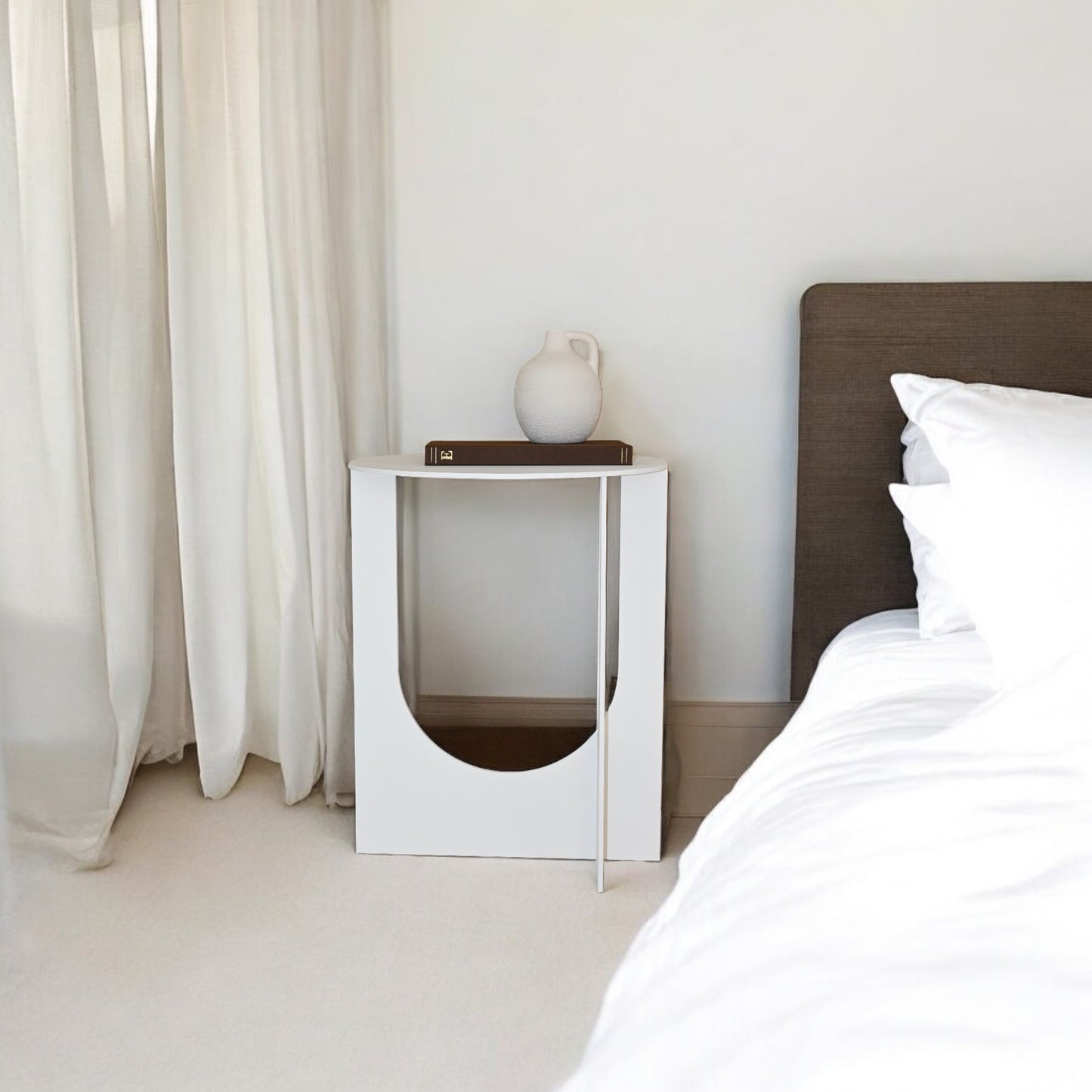 Mesa Cirat vista frontal con libro y jarroncito en parte superior junto cama de dormitorio