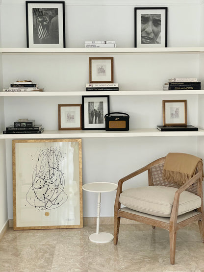 Mesa auxiliar Gorga junto a sillón de comedor, al lado de un cuadro bajo una estantería