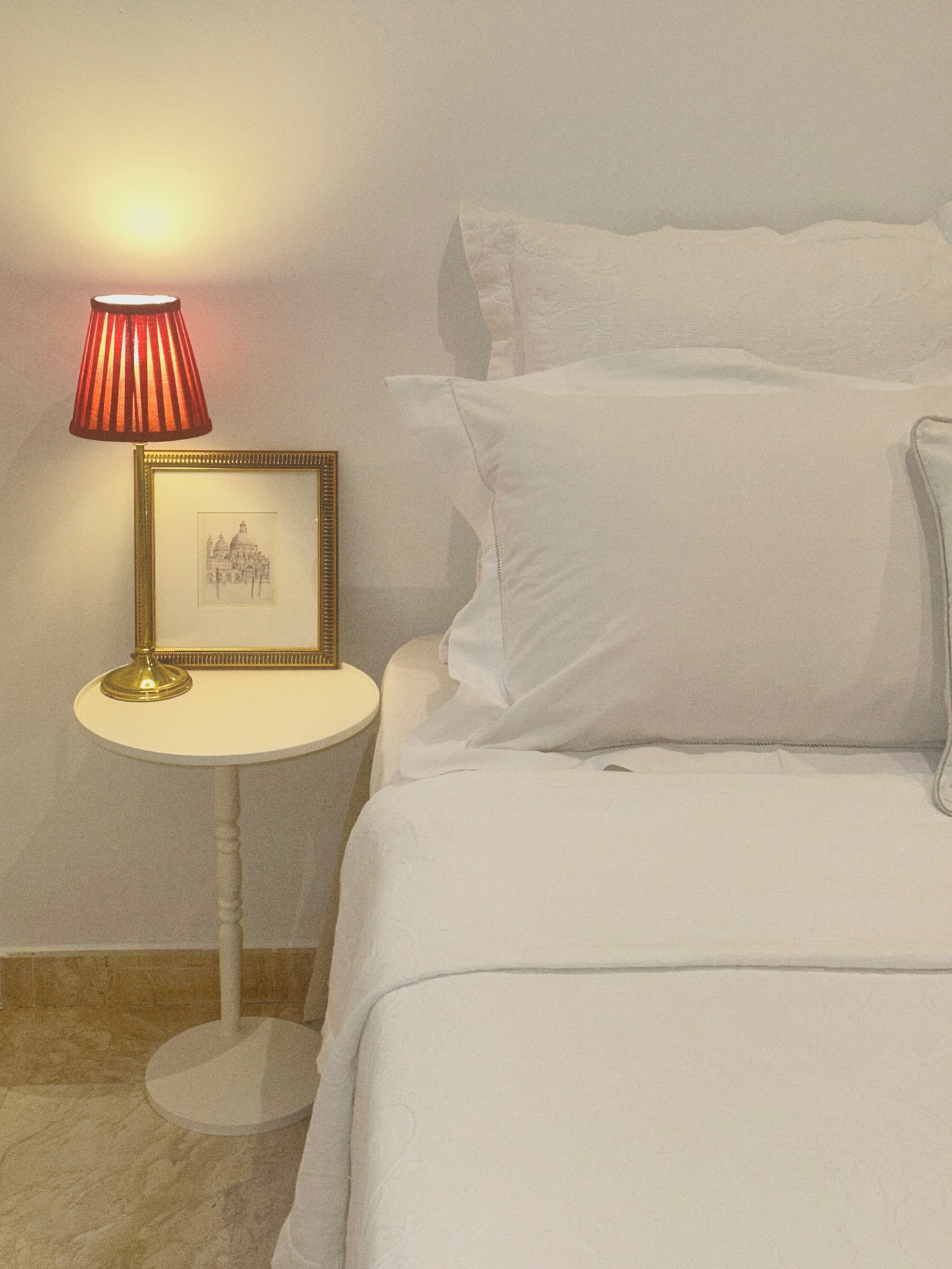 Mesa modelo Gorga con una lámpara y una decoración encima junto a una cama con almohadas